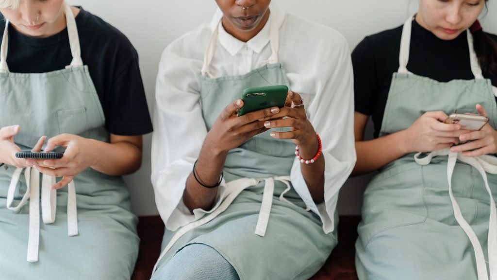 three women in aprons looking at mobile phones