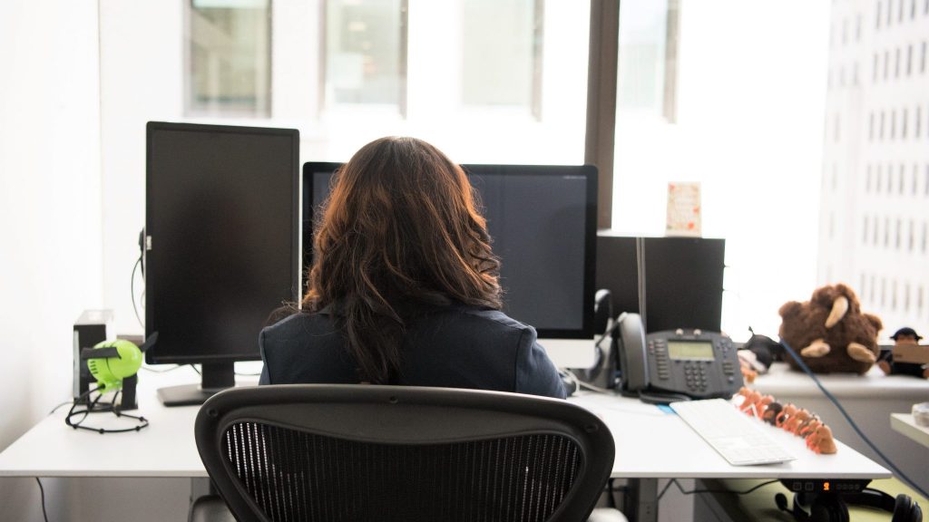 woman sitting at office computer screen and other electronic audio devices