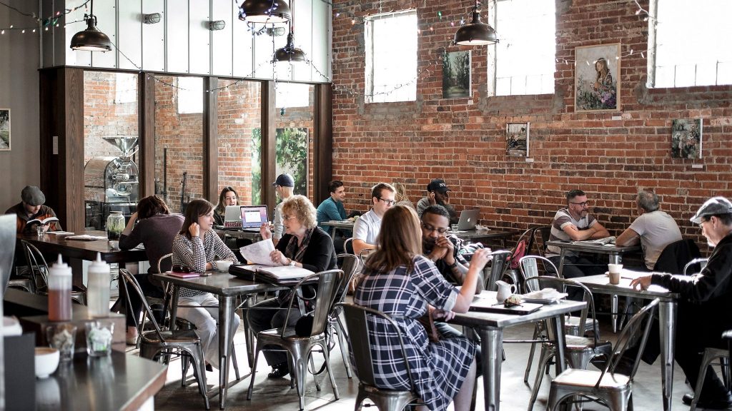 people sitting a metal tables in crowded cafe as an example of where people could benefit from speech-in-noise testing