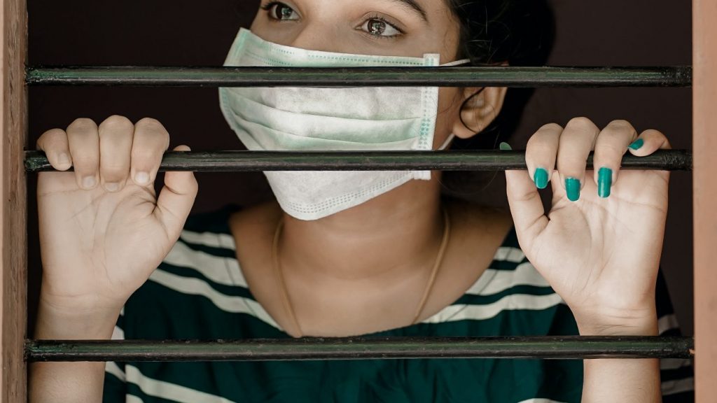 woman wearing face mask grasping prison bars to represent a minefield of disconnection
