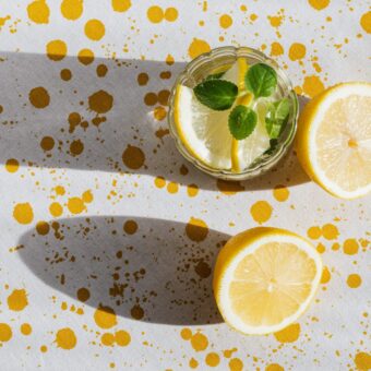 glass of lemonade and a sliced lemon on a white table speckled with yellow