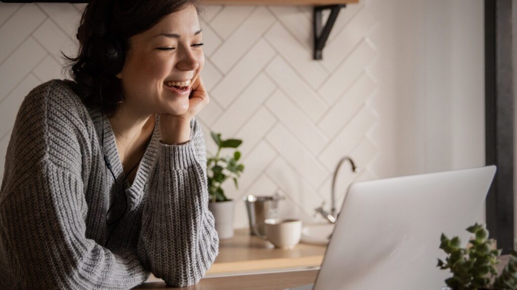 woman sitting at kitchen counter smiling at open laptop computer to represent virtual aural rehab training